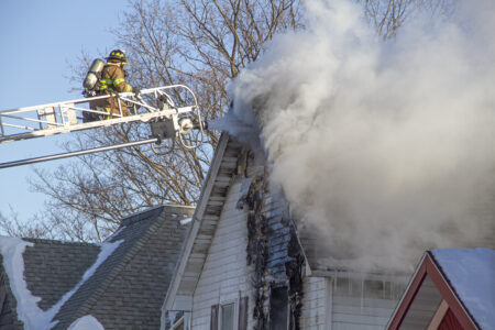 Escanaba Public Safety's Det. Lt. Tabitha Turnacliff is at the top of ladder truck 35 with a jet spraying the peak of a burning house.